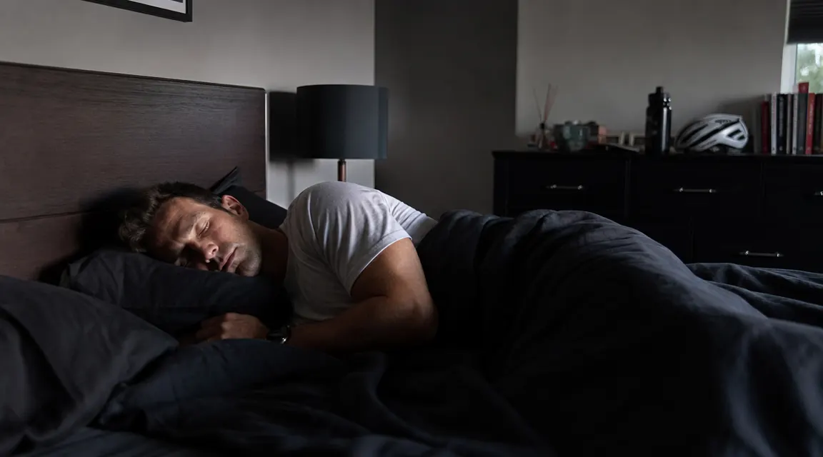 Athlete sleeping soundly in a dark bedroom, recovery context after an evening training session